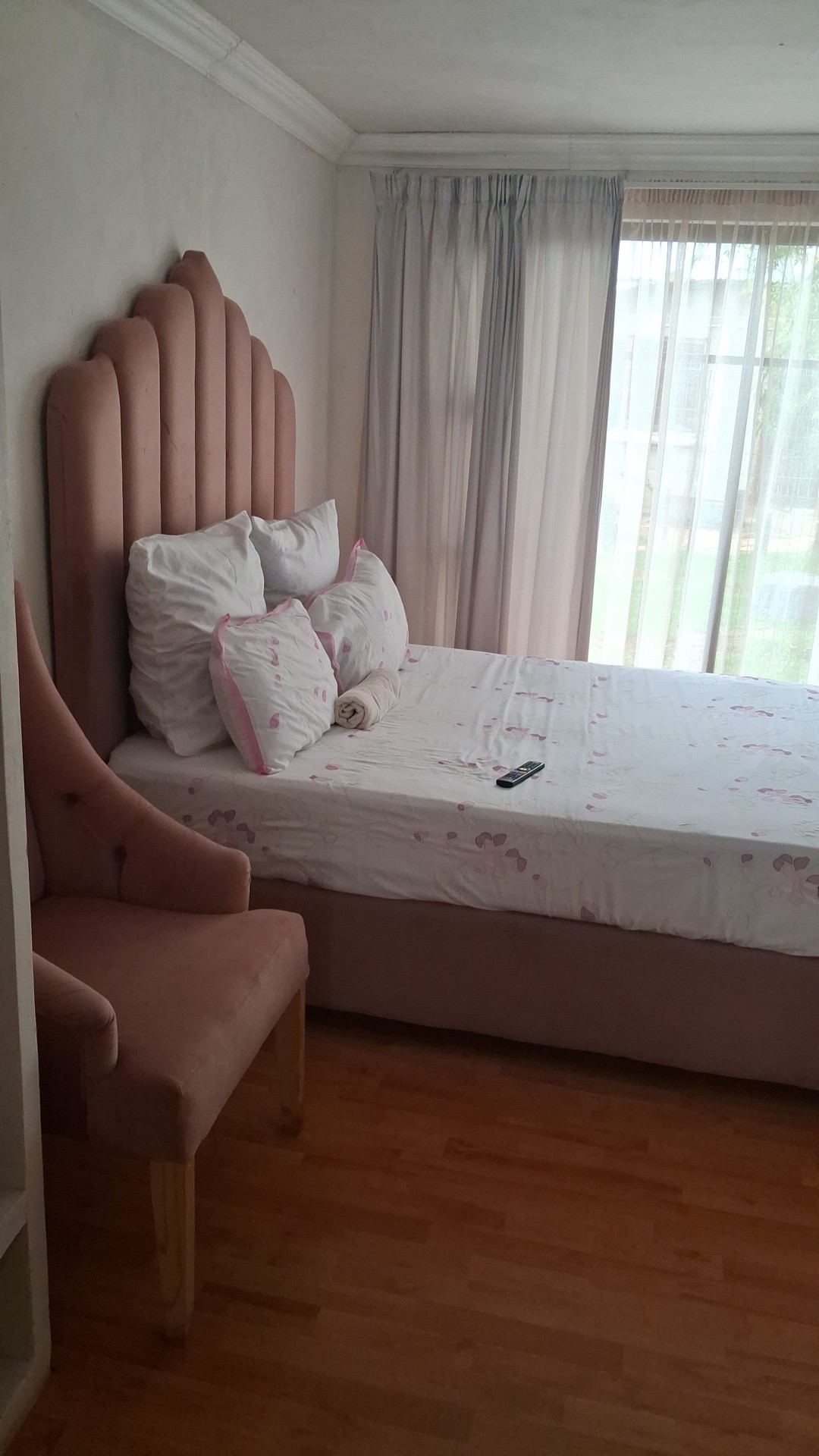 Pink scalloped headboard with pink chair and wooden floor